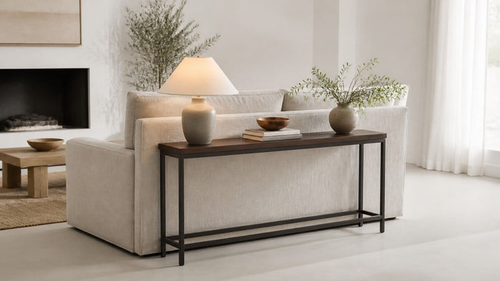 Mid-century modern wood console table behind a sofa with lamp and decor on white background in professional studio lighting