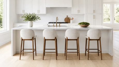 Modern bar stools and counter stools arranged neatly along a bright white kitchen island with a countertop overhang, illustrating comfortable seating spacing and style variety.
