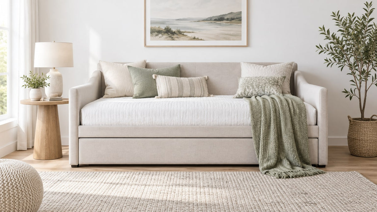 Bright neutral bedroom featuring a stylish upholstered daybed with pull-out trundle, side table, lamp, pillows, and area rug