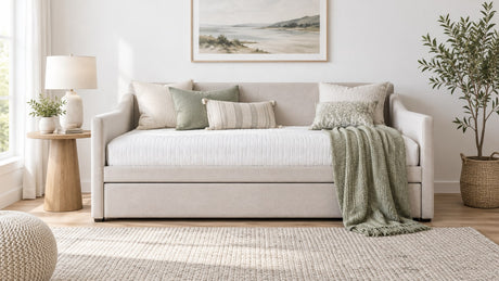 Bright neutral bedroom featuring a stylish upholstered daybed with pull-out trundle, side table, lamp, pillows, and area rug