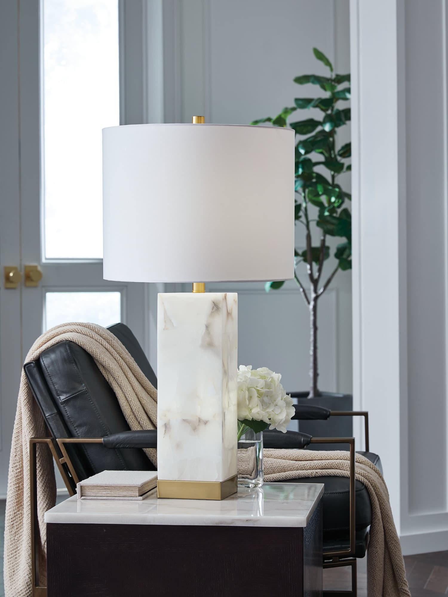 Linderfield white alabaster and goldtone table lamp illuminated on side table